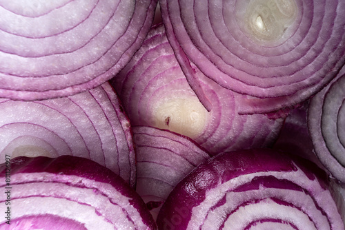 Slices of red onion neatly arranged on a white background. The vibrant purple tones and intricate rings create a visually appealing pattern. The translucence adds depth and texture to the composition.