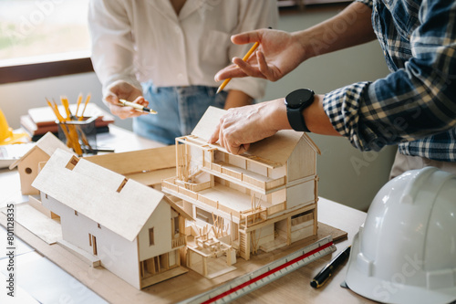 Close up shot of scale model house on table with architects. Two architects making architectural model in office together. to form a new building..