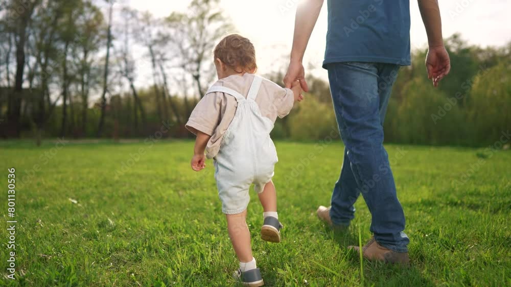 baby toddler and father take their first steps for a walk in the park. happy family kid dream concept. baby and father together walk hand in hand on the grass in the summer in the park sunset baby toddler and father take their first steps for a walk in the park. happy family kid dream concept. baby and father together walk hand in hand on the grass in the summer in the park sunset