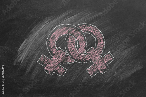 Two female gender symbols, sketched with pink chalk, overlap on a dark classroom chalkboard. LGBT concept