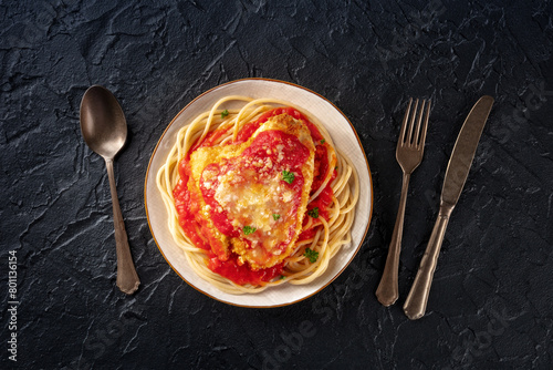 Chicken Parmesan, Italian pasta dish. Breaded chicken breast with cheese and spaghetti with tomato sauce, top shot on a black stone background with silverware