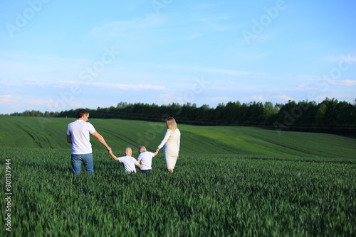 Features a lovely family consisting of a man, a woman, and a child. They are posing for a photograph in a lush green field, creating a beautiful and natural backdrop. The man is holding the child's