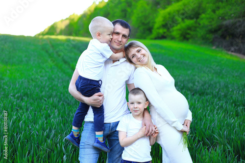 A man standing with two young boys in a field and pregnancy woman. Family expecting their third child. Their smiles reflect the happiness and joy they are experiencing in this moment. The lush green