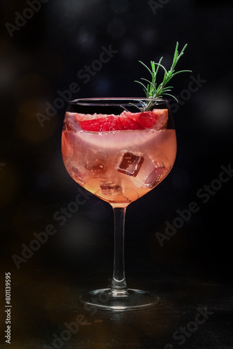 Fancy cocktail with fresh fruit. Gin and tonic drink with ice at a party, on a black background. Alcohol with pink grapefruit and rosemary, toned image