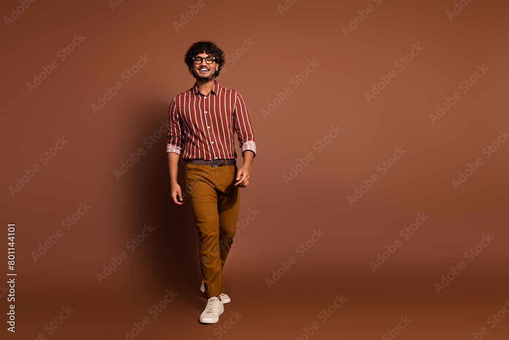 Fototapeta premium Full size photo of nice young man walk empty space wear striped shirt isolated on brown color background