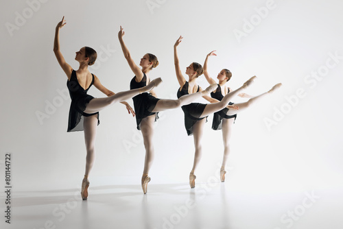 Graceful ballet performance. Four graceful ballet dancers, teens in black leotards and pointe standing in md-pose, practicing against grey studio background. Concept of ballet art, dance studio, youth