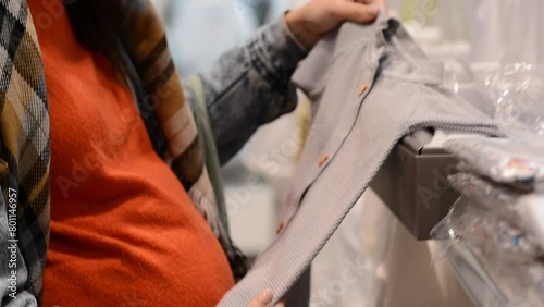 Pregnant woman choosing newborn clothes at baby shop store. Children clothing store, sale. Pregnancy and expectation concept.