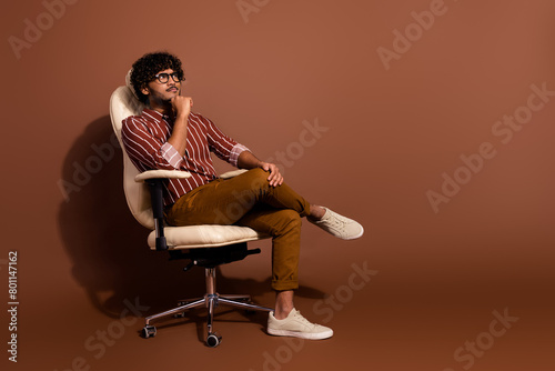 Full size photo of nice young man sit chair look empty space wear shirt isolated on brown color background