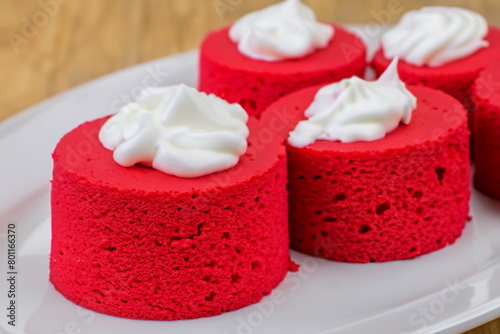 red cakes. small red round cakes with white cream lie on a white plate, close-up, sweet concept