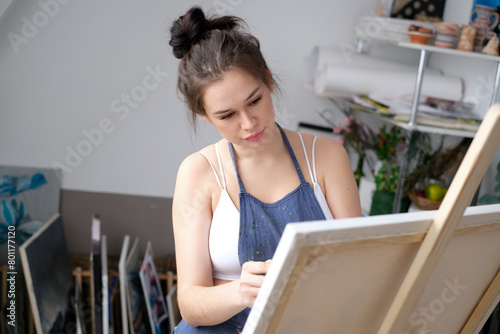 Young female artist paints a picture with oil on canvas in art studio