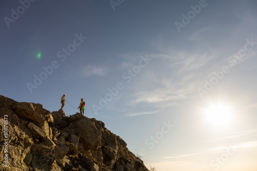 Two people standing on a rocky mountain top, looking out at the horizon