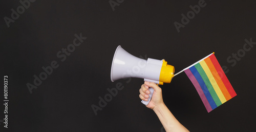 Hand is hold Rainbow pride flag and megaphone on black background.