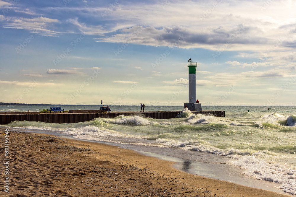 Rough waves crashing into the shore and the lighthouse pier in Grand Bend, on a summer evening, Ontario, Canada.