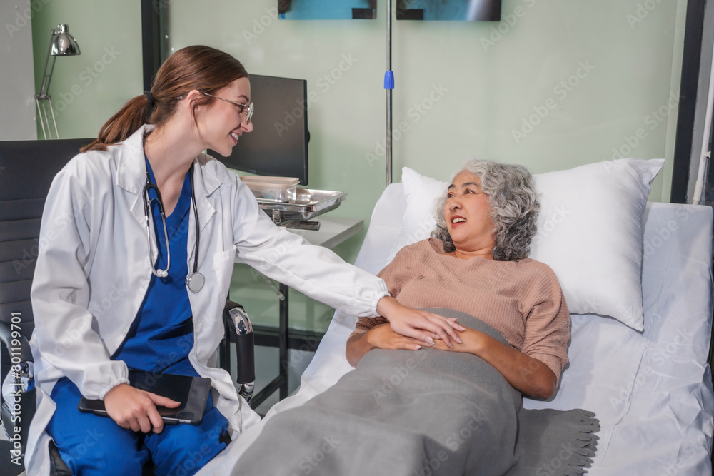 Caucasian female specialist doctor attends to an elderly Asian female patient in a hospital bed, providing medical care and support. Caucasian female specialist doctor attends to an elderly Asian female patient in a hospital bed, providing medical care and support.