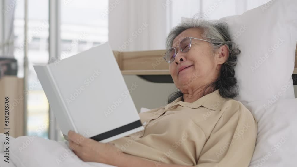 Side view, Handheld medium shot, Happily Asian aged woman wearing glasses lying on bed and enjoy reading book, Yawn with sleepy, Closed her eyes to sleeping Side view, Handheld medium shot, Happily Asian aged woman wearing glasses lying on bed and enjoy reading book, Yawn with sleepy, Closed her eyes to sleeping