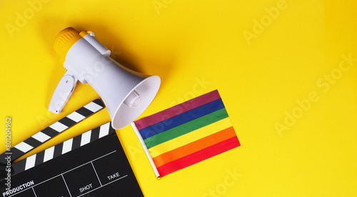 Clapper board and rainbow pride flag and megaphone on yellow background.
