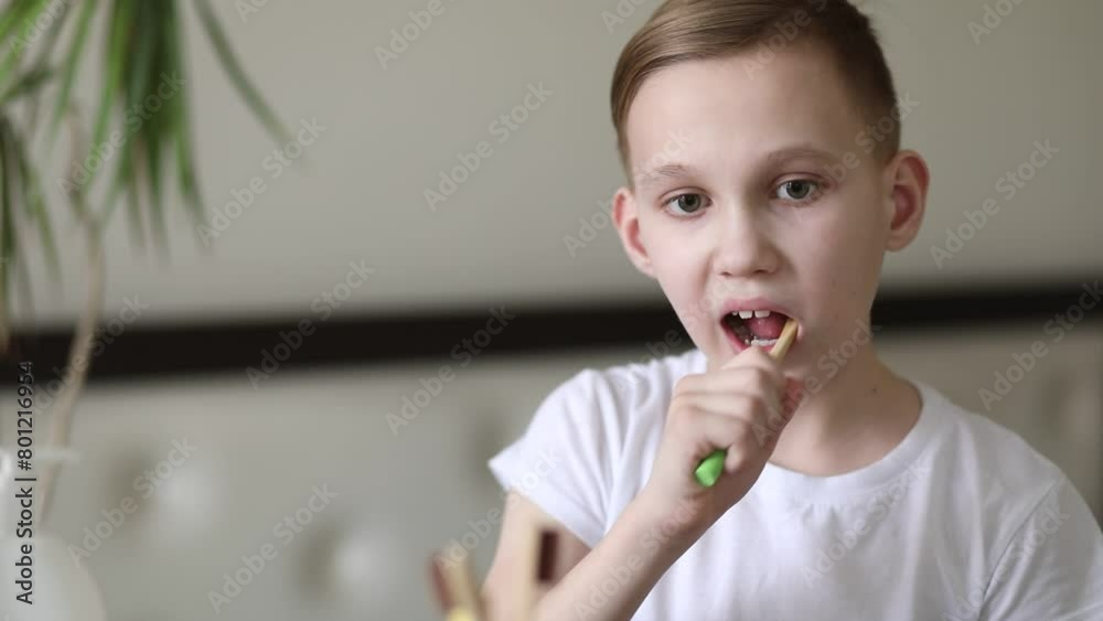 Smiling blonde teenager kid boy brushing teeth at home looking in small mirror. Morning routine. Smiling blonde teenager kid boy brushing teeth at home looking in small mirror. Morning routine.