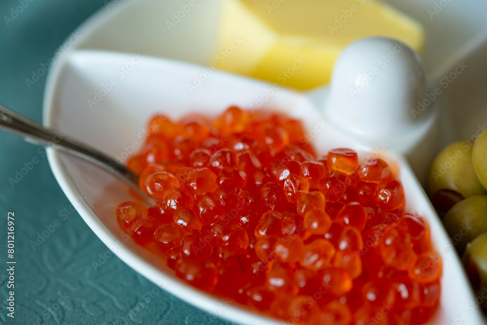 Red caviar in a white plate with olives, cheese and spoon