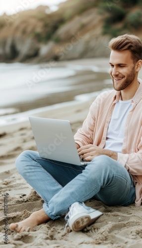 Young man in casual attire working remotely on laptop at the beach, freelancing lifestyle