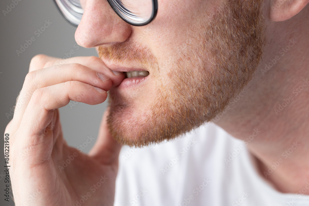 Fototapeta premium Brooding man in glasses chewing on his fingernails. Fingernail biting.