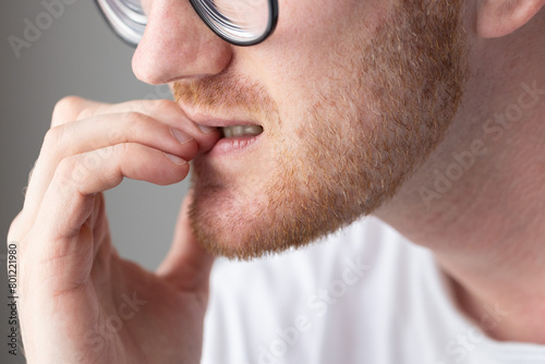 Brooding man in glasses chewing on his fingernails. Fingernail biting.