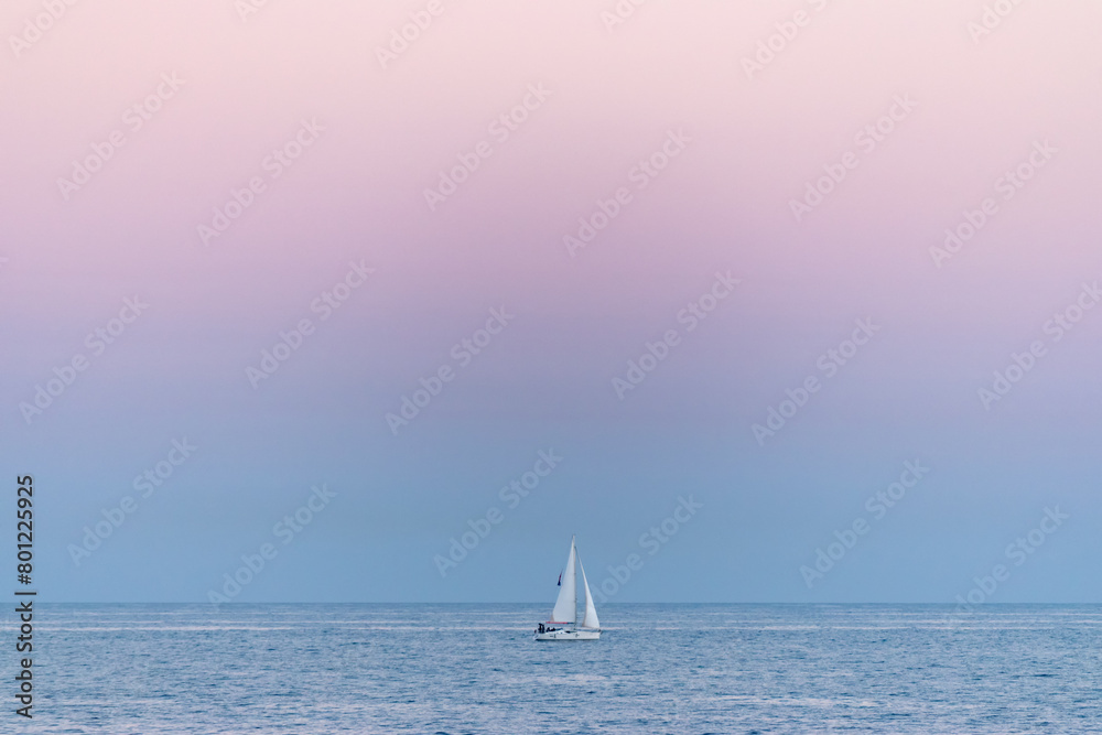 Obraz premium White sailboat at the beautiful blue sea during sunset.