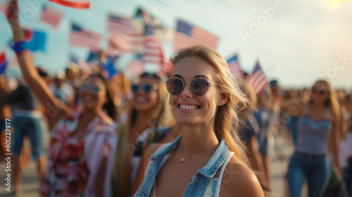 American woman at outdoor event; crowd holding American flags.