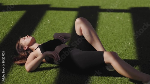 Attractive, slim, athletic girl, model, woman, lying posing on a green lawn with contrasting striped light, summer, sunny atmosphere, contrast, black sportswear, stretching, relax, sport life photo