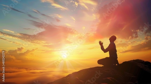 Silhouette of a person kneeling with his arms open and looking at the sky at sunset