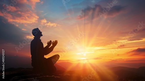 Silhouette of a person kneeling with his arms open and looking at the sky at sunset