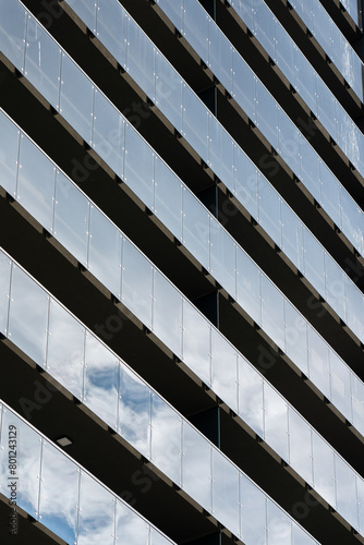 Modern residential building facade. Symmetrical balcony strips reflecting blue sky.