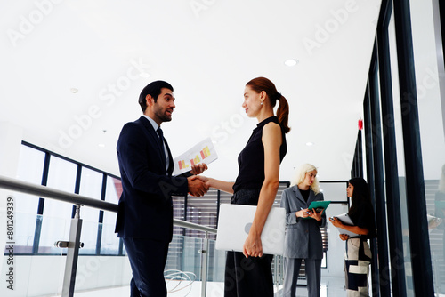 Business man holding hands, business woman standing and smiling.