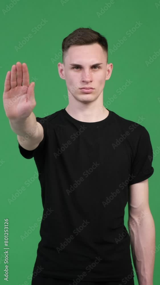 Focused Caucasian man showing stop sign with palm in denial on green background. Disagreement and rejection concept. Vertical video.