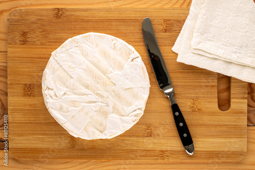 Brie cheese with a clay plate and a knife on a wooden table, macro, top view.