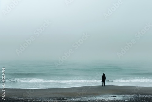 Man standing alone on beach looking out at foggy sea