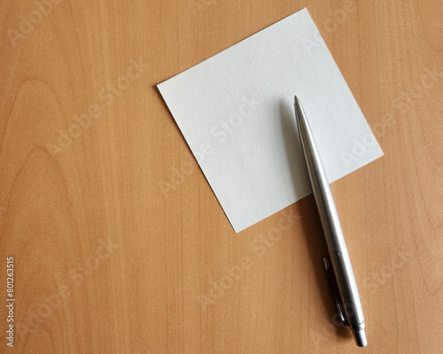 a piece of paper for notes on the background of a wooden table. with a metal ballpoint pen, a place for a text message or multimedia content. image is for viewing from above. empty notes.