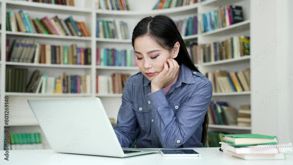 Asian female student bored doing homework while sitting at university library. Exhausted young woman is too lazy to study on a laptop computer. Overworked applicant is preparing for entrance exams Asian female student bored doing homework while sitting at university library. Exhausted young woman is too lazy to study on a laptop computer. Overworked applicant is preparing for entrance exams