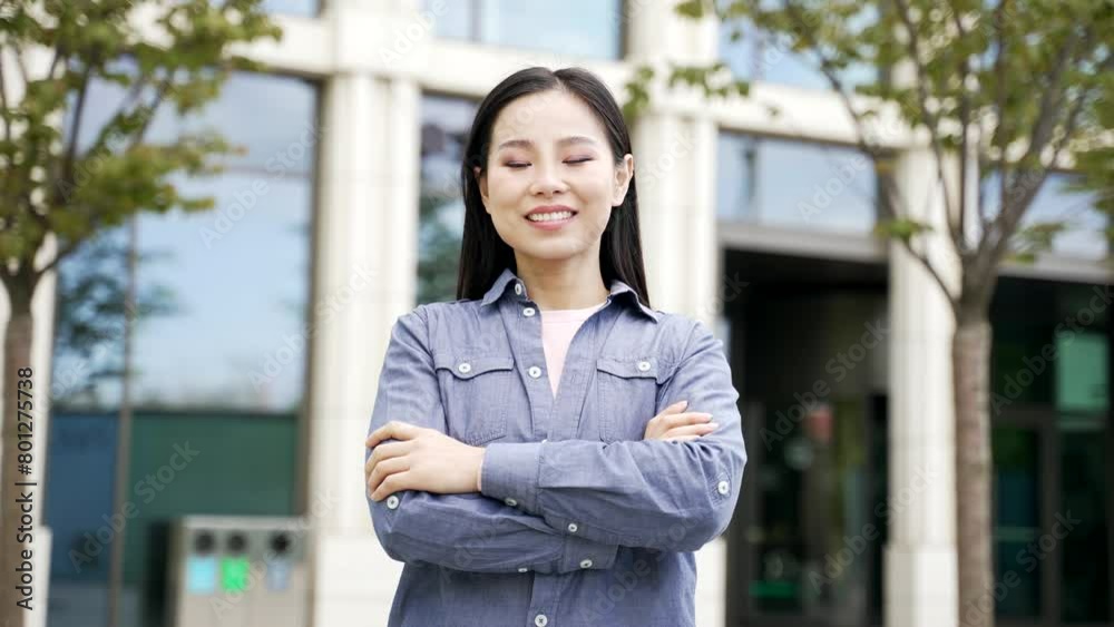 Portrait of smiling asian female student standing on the street on campus space near university building. Head shot of happy young beautiful woman applicant posing with crossed arms looking camera Portrait of smiling asian female student standing on the street on campus space near university building. Head shot of happy young beautiful woman applicant posing with crossed arms looking camera