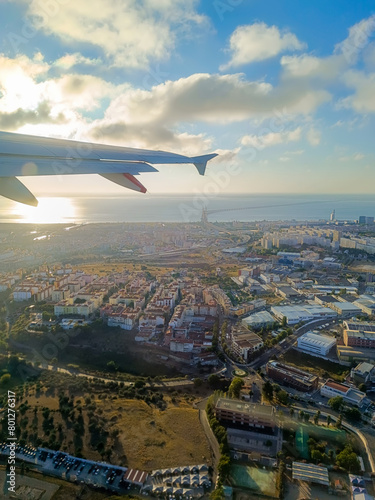Airplane wing backlit by the rising sun flying over Lisbon with the architecture in aerial view and the Vasco da Gama bridge over the Tejo river on the horizon, PORTUGAL photo