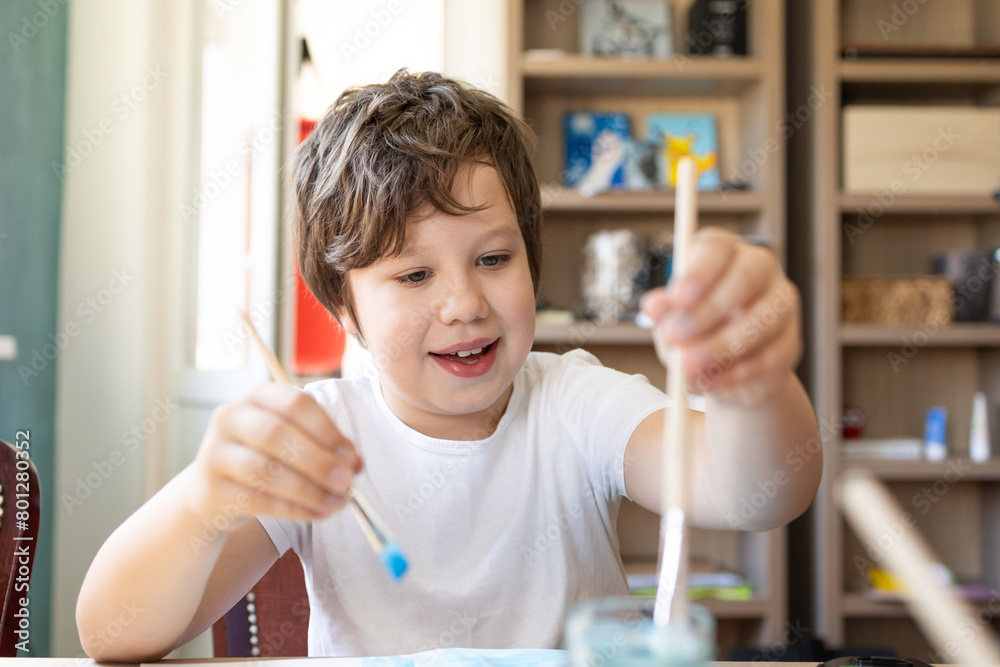 A young boy, bathed in sunlight, meticulously wields his watercolor brush, each stroke a dance of vibrant hues on his canvas. Immersed in his art, he expresses a world of imagination and emotion, each