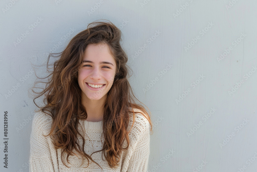 Happy young woman with blowing hair standing in front of gray wall smiling in the wind Happy young woman with blowing hair standing in front of gray wall smiling in the wind