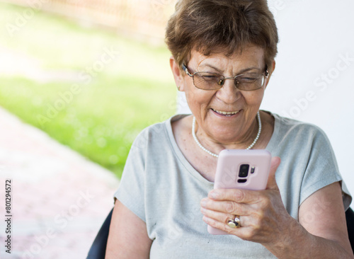 One elderly woman is smiling while using her cell phone. On the video call with her family. Reading beautiful wishes for birthday 