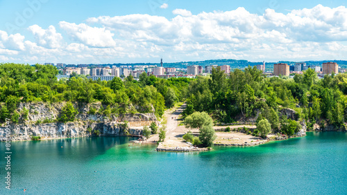 View of Lake Zakrzówek with apartment buildings in the background. Locals swimming in the crystal water which fills the old quarry in Kraków, Poland.