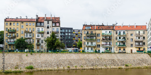 The Oder River runs straight through Wrocław, Poland. A mix of older and newer apartment buildings run along parts of the brown river.