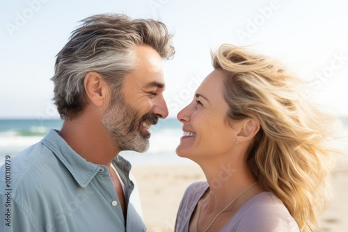 An adorable mature Caucasian couple on a sunny beach date. While on vacation, a happy couple kisses with noses touching.