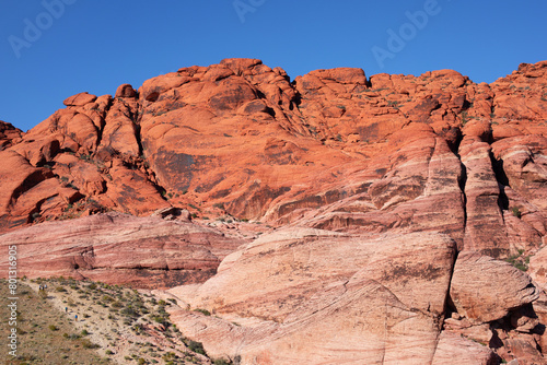 USA, Nevada, Red Rock Canyon. falaisee à la roche rouge et bariolée de Red Rock Mountain dans un canyon aride d'un désert poussiéreux aux buissons secs.