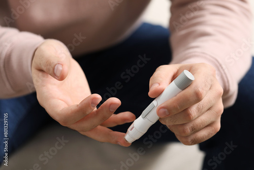 Diabetes test. Man checking blood sugar level with lancet pen on blurred background, closeup