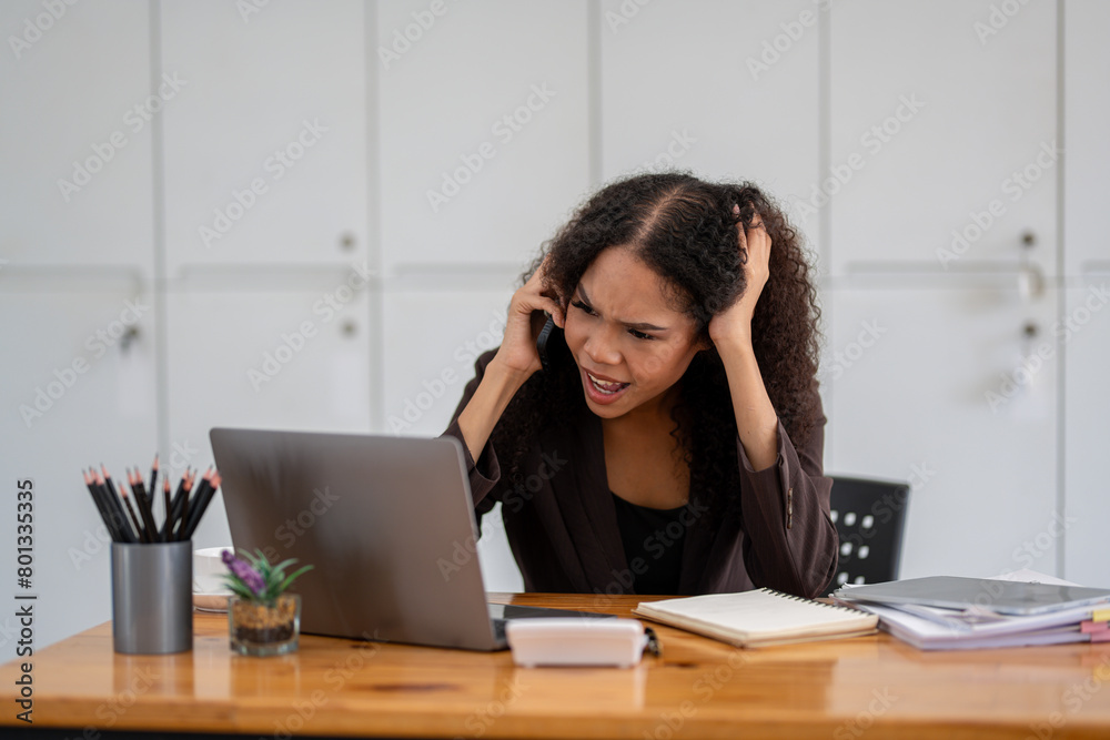 Cheerful African American businesswoman having a phone conversation while working on a laptop in a modern office. Cheerful African American businesswoman having a phone conversation while working on a laptop in a modern office.