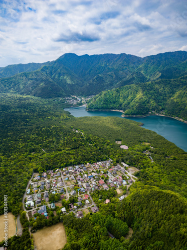 Small village surrounded by lush forest and rugged mountains next to a lake (Saiko, Japan) © whitcomberd