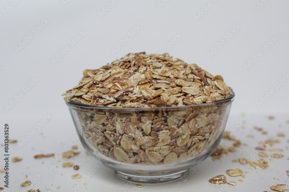 Rolled oats in transparent glass bowl, isolated on white background